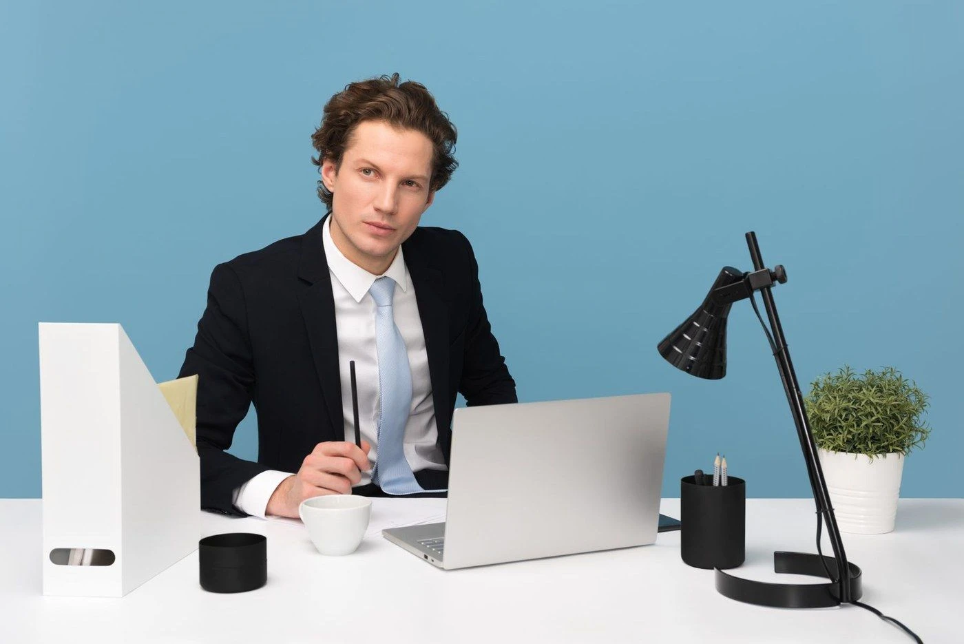 A man at a tidy desk with a laptop and a lamp