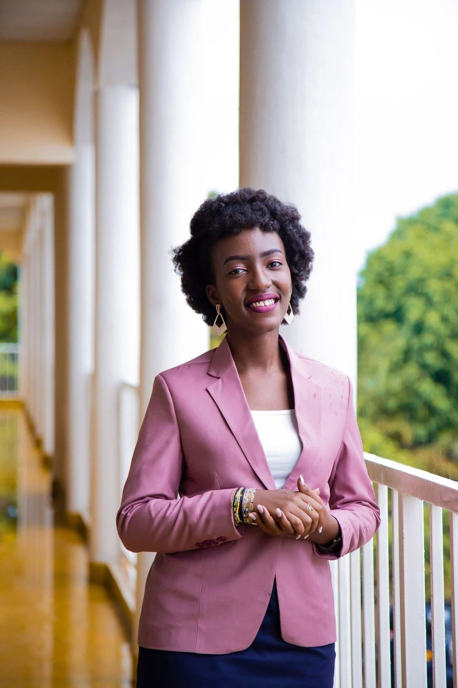 A woman in a pink blazer smiling on a porch