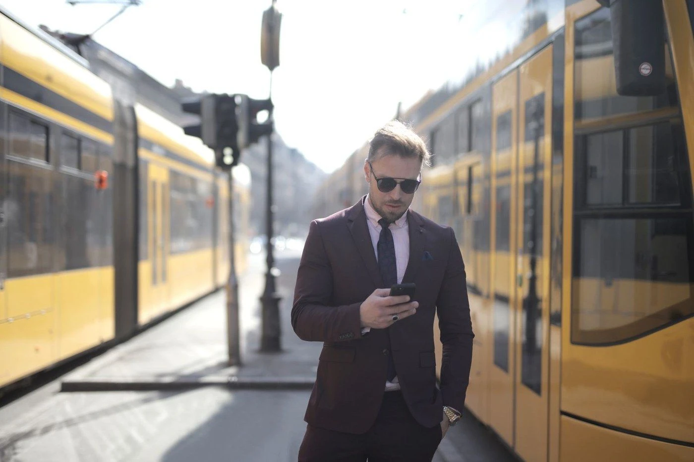 A man in a suit reading his phone while a tram passes