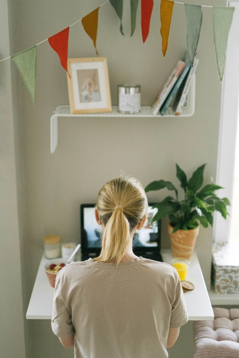 A woman seen from behind at a desk with a laptop and plants