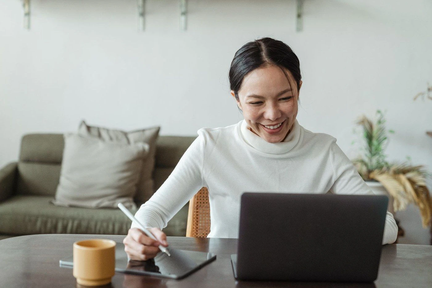A woman smiling at her laptop while writing a note