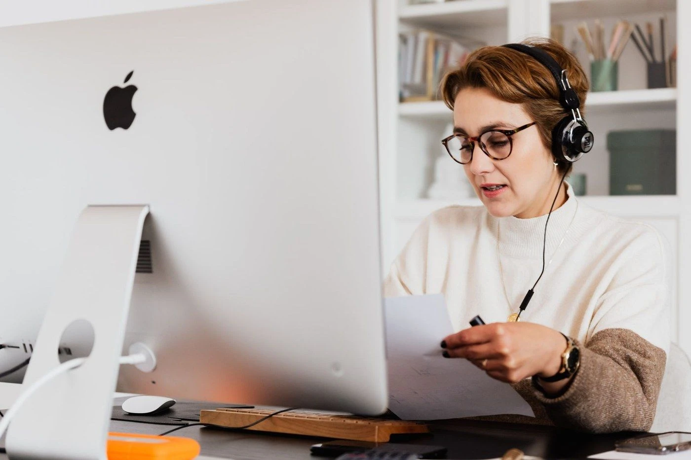 A woman in glasses talking on a headset at a computer