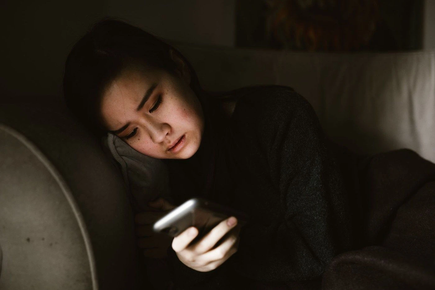 A woman in a dark room lit by her phone