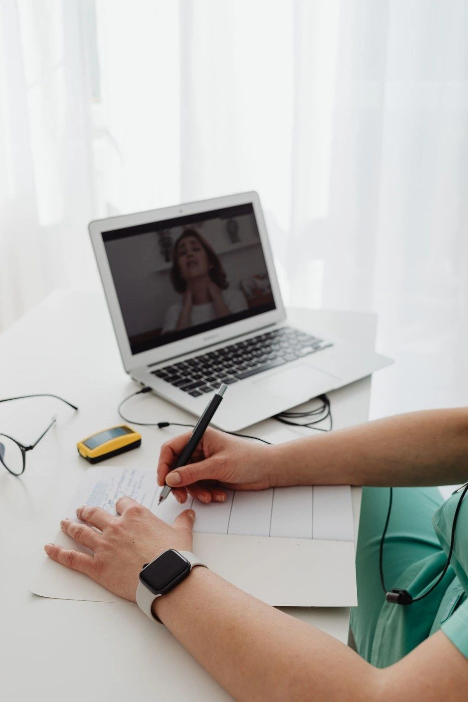 A laptop on a video call beside a hand taking notes