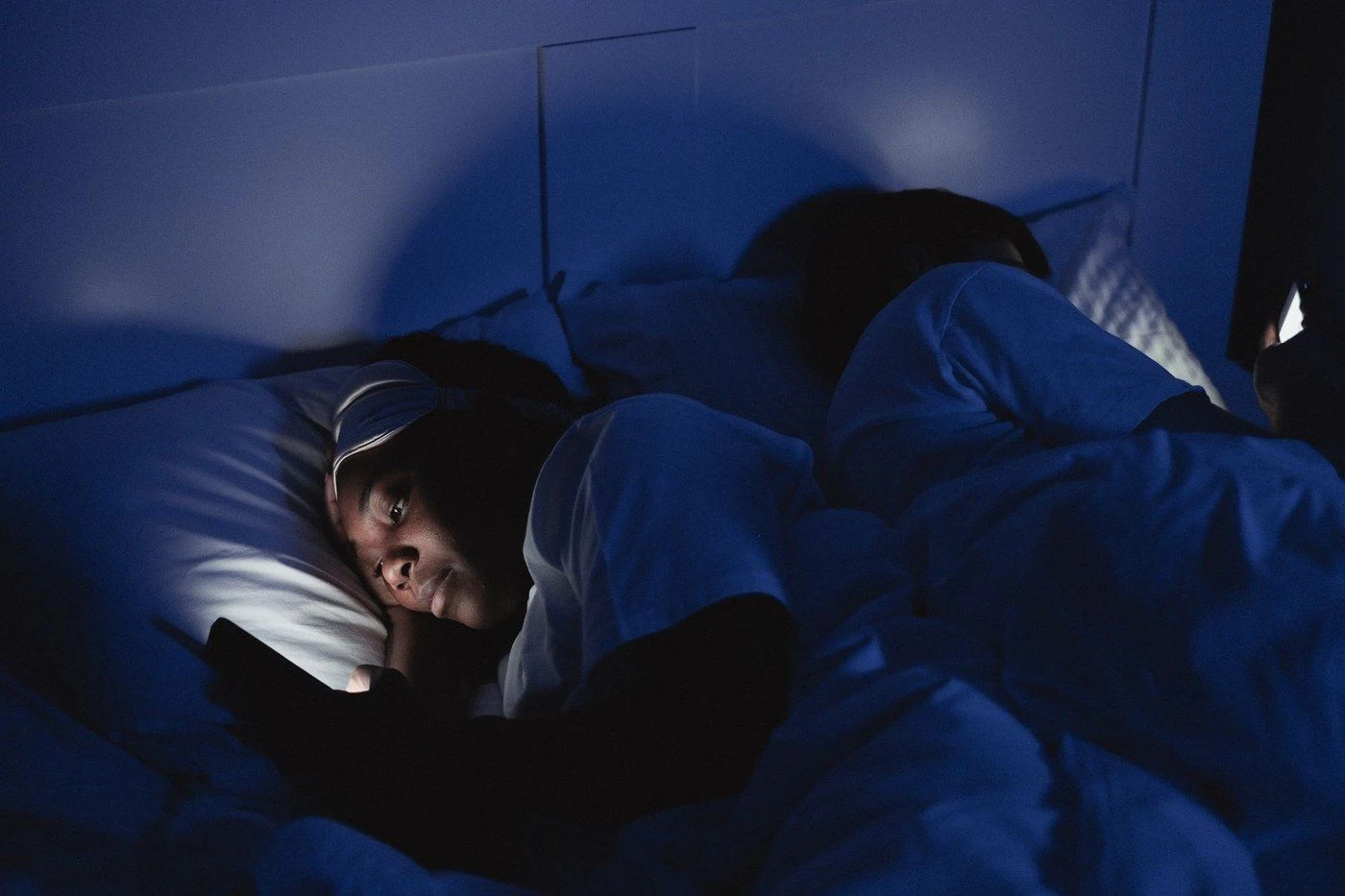 A person under a blue duvet looking at a phone at night