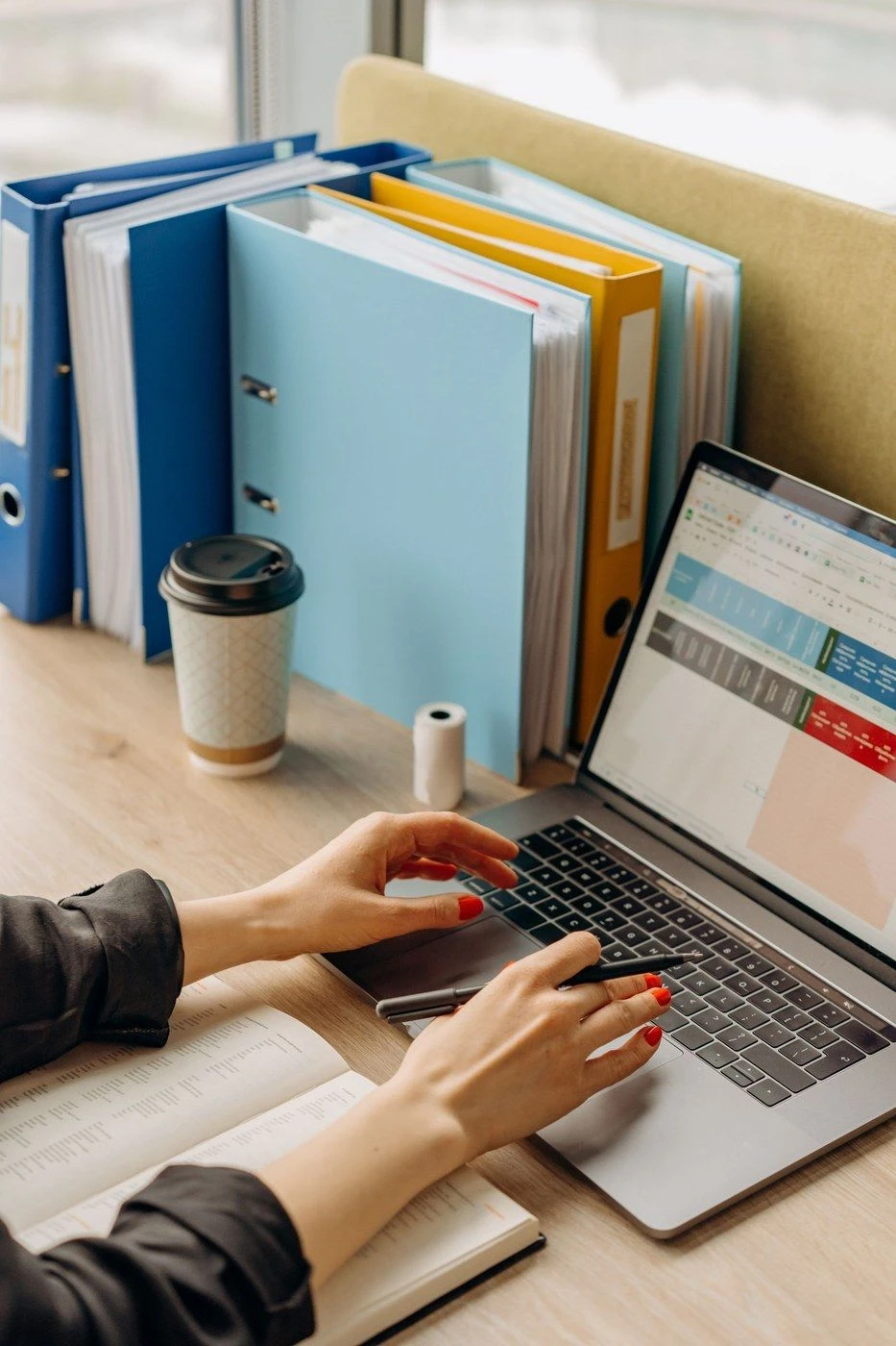 A hand on a laptop beside a coffee cup and folders