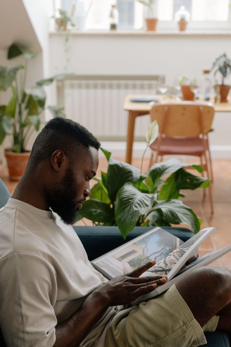 A man reading on a sofa in a plant-filled room