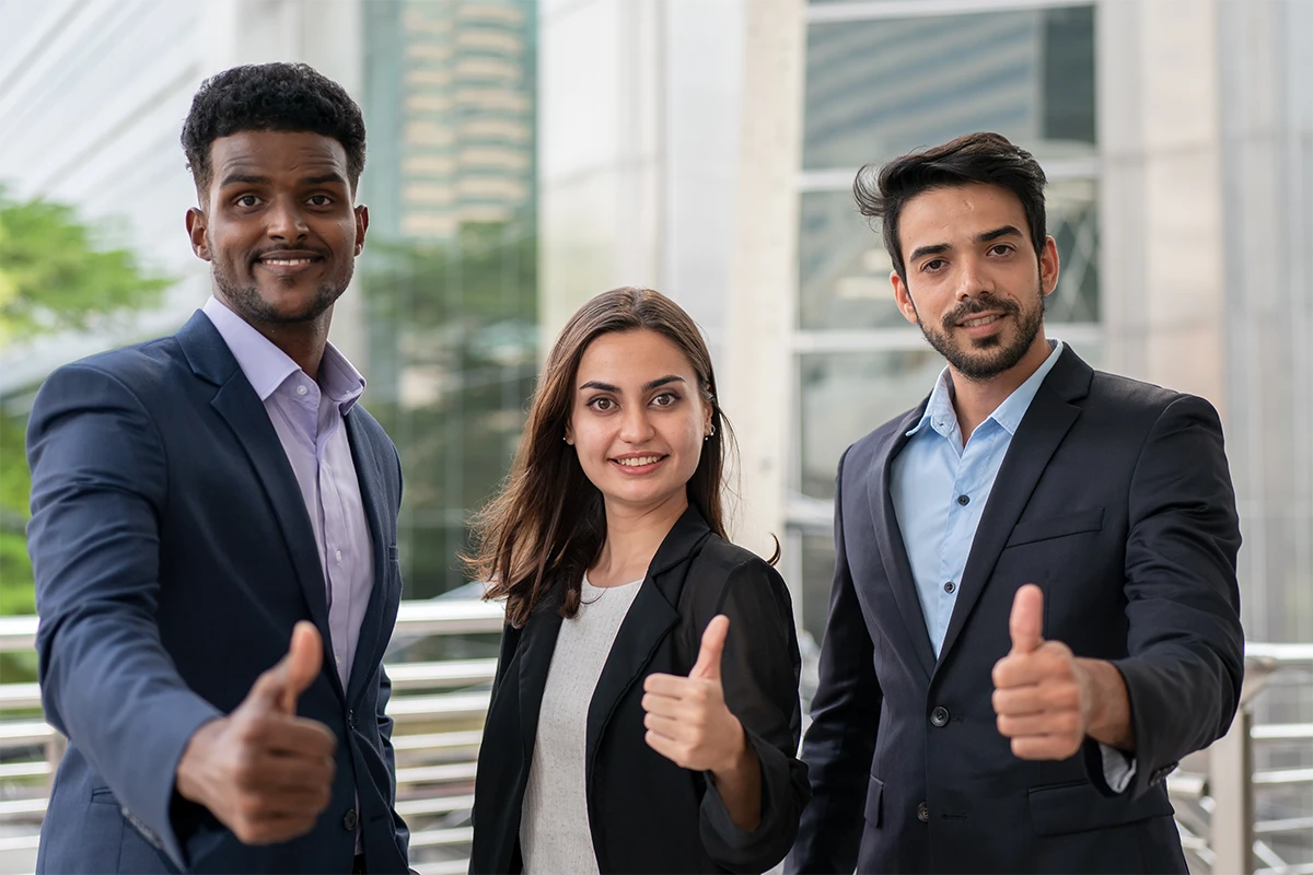 Three colleagues in business dress outside an office, giving a thumbs up